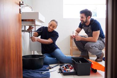 Male and female apprentice plumbers fixing a sink