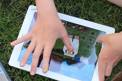 Childs hands on the screen of a tablet, playing Minecraft